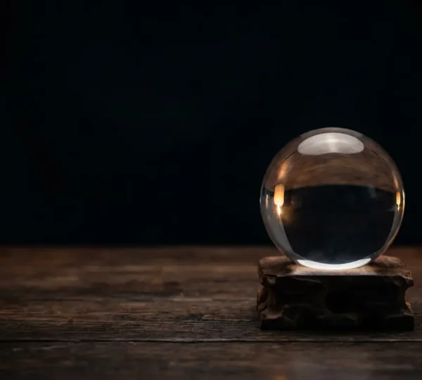 Una sfera di quarzo ialino su supporto in legno scuro illuminata da candele su sfondo scuro